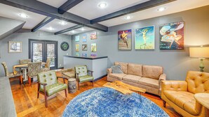 A spacious living room with a high ceiling, wooden beams, a dining area with chairs and a table, and a large blue rug.