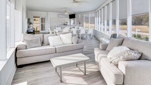 Ein geräumiges Wohnzimmer mit grauem Sofa, einem weißen Couchtisch und einem Essbereich mit weißen Stühlen.