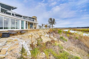 A modern building with large windows, a stone patio with outdoor seating, and a view of a river. - Luxury Lakefront Retreat w/ Dock in Runaway Bay (Bridgeport)
