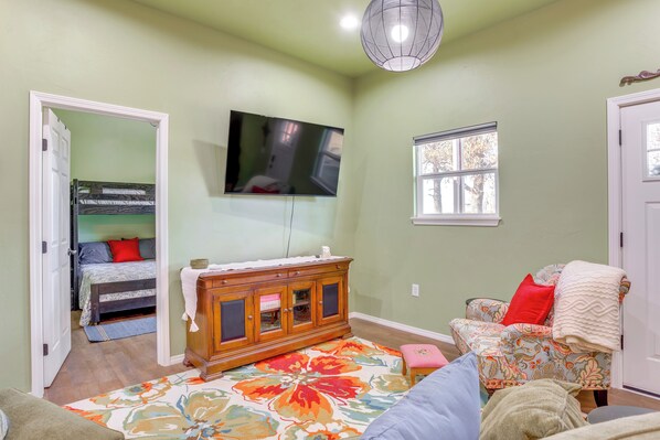 A room with a bunk bed, a television mounted on the wall, a floral-patterned rug, and a chair with a blanket. - 4 Mi to Lazy E Arena: Horse Lover's Haven w/ Grill (Guthrie)