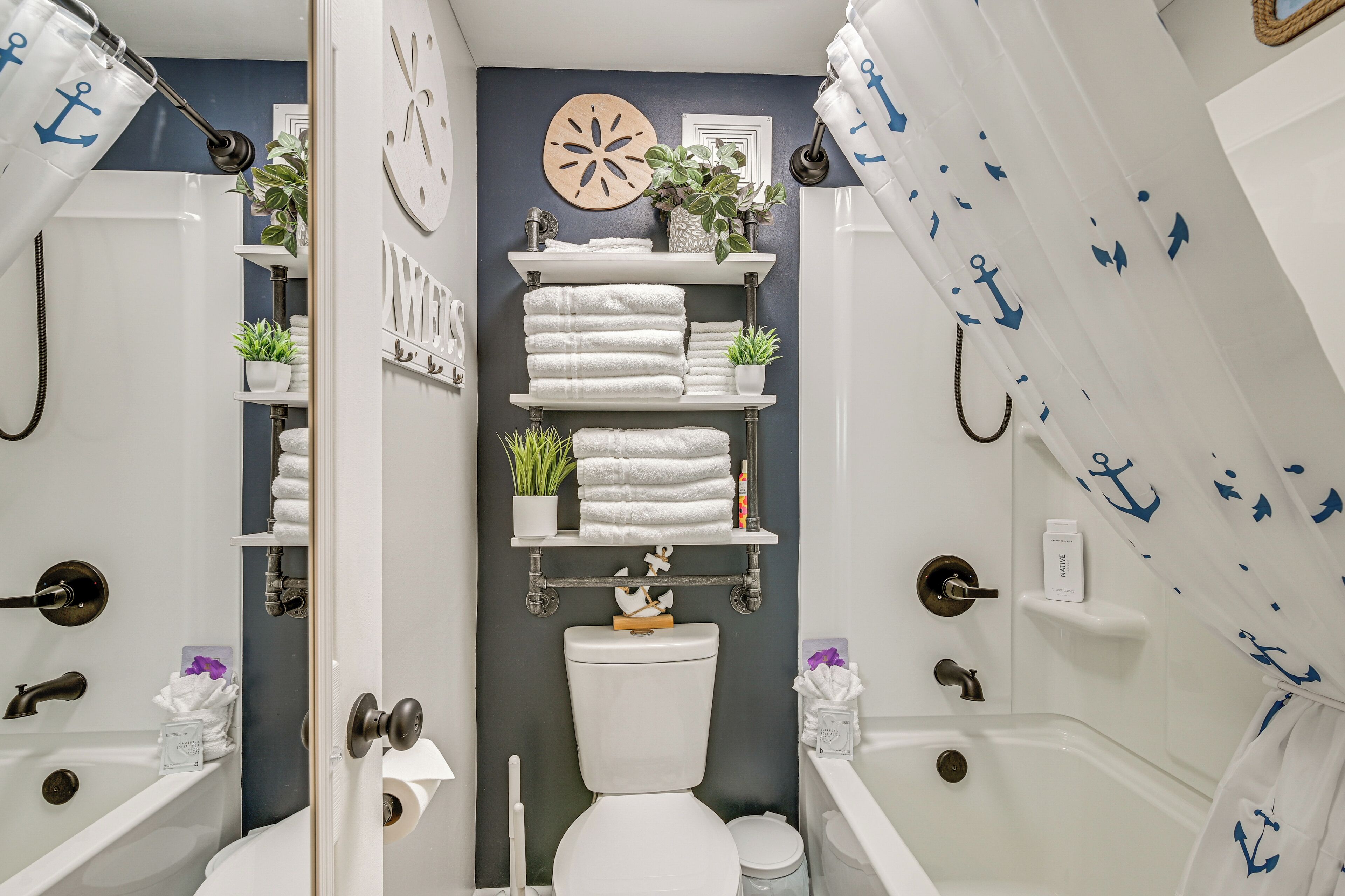 A bathroom with two white bathtubs, a toilet, and shelves with towels and plants.