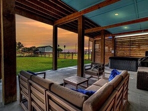 An outdoor patio with wooden furniture, a barbecue grill, and a view of a grassy field and distant buildings. - Nautical Nest 2 Bedroom Home (Rockport)