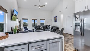 A spacious living area with a large island, a modern kitchen with a stainless steel refrigerator, and a ceiling fan. - Nautical Nest 2 Bedroom Home (Rockport)