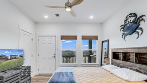 A bedroom with a bed, a television, a ceiling fan, and a large window. - Nautical Nest 2 Bedroom Home (Rockport)