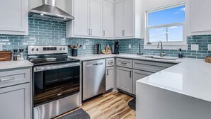 A modern kitchen with white cabinets, a stainless steel range hood, and a blue-tiled backsplash. - Nautical Nest 2 Bedroom Home (Rockport)