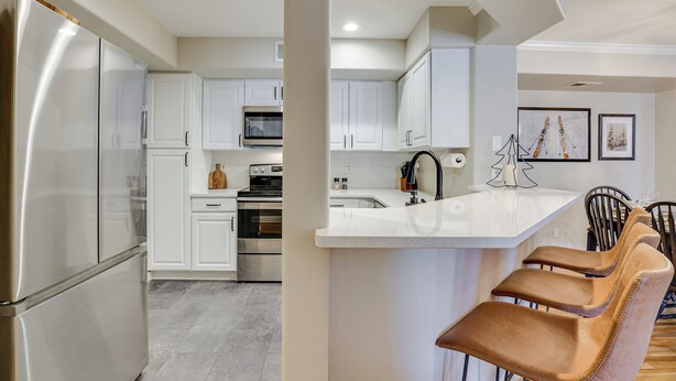 Una cocina moderna con electrodomésticos de acero inoxidable, armarios blancos y una isla central con taburetes de bar.
