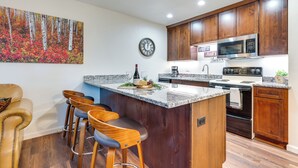 A modern kitchen with wooden cabinets, a granite countertop, a stainless steel microwave, and a bar area with stools.