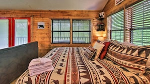 Une chambre de style cabane avec des murs en bois, un lit avec une literie à motifs, une porte rouge et une pancarte sur laquelle on peut lire : « Cabane, douce cabane ».
