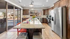 A modern kitchen with a large island, stainless steel appliances, and sliding glass doors leading to an outdoor patio. - Splash Pad Place #29 3 Bedroom Home (Ivins)