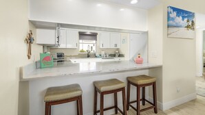 Una cocina con armarios blancos, encimera de mármol y tres taburetes de madera.