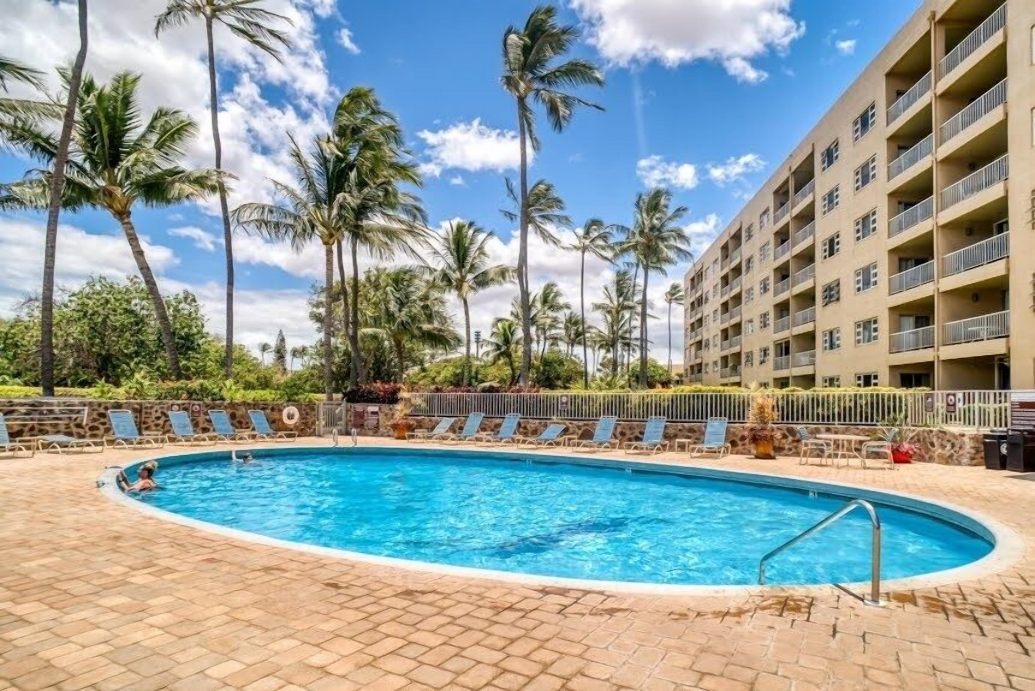A swimming pool surrounded by palm trees and a multi-story building with balconies.