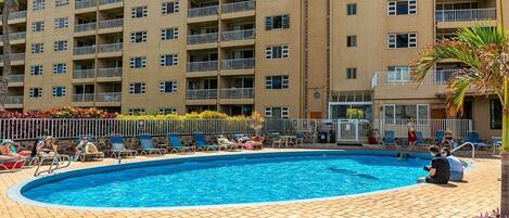 A swimming pool with lounge chairs and a multi-story building in the background.