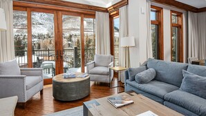 A spacious living room with a grey sofa, armchairs, and a coffee table. Large windows offer a view of a snowy mountain landscape. - Ritz Carlton Vail #402 4 Bedroom Condo (Vail)