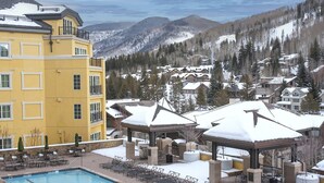 A yellow building with a pool and outdoor seating, surrounded by snow-covered mountains and trees. - Ritz Carlton Vail #402 4 Bedroom Condo (Vail)