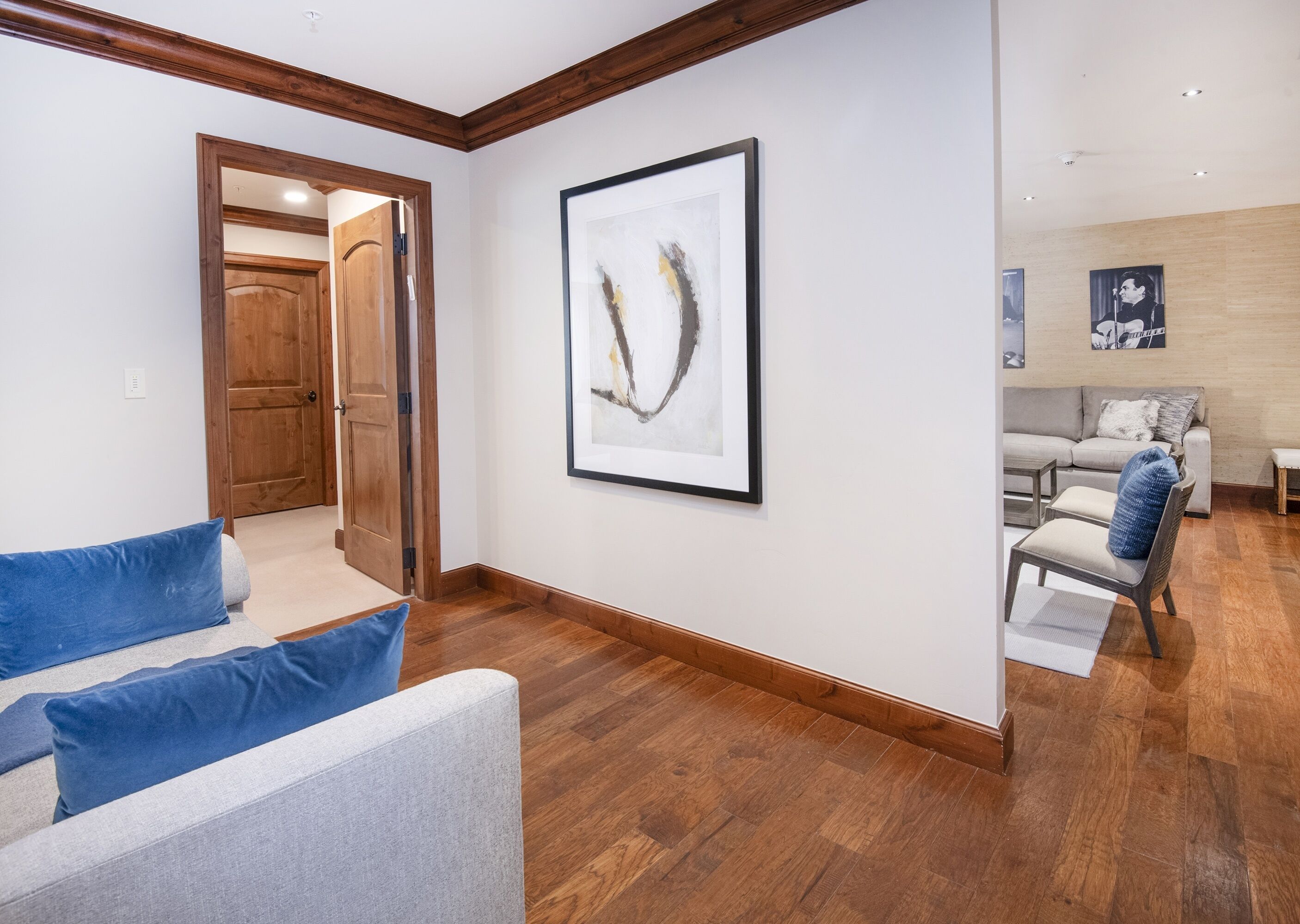 A modern living room with a grey sofa, blue cushions, a framed abstract painting, and a wooden floor.