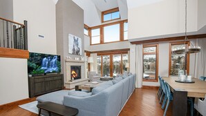 A spacious living room with a large grey sectional sofa, a wooden dining table with blue chairs, a fireplace, and a TV. - Ritz Carlton Vail #402 4 Bedroom Condo (Vail)