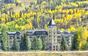 A multi-story hotel with a prominent tower, surrounded by a forested area with yellow foliage. - Ritz Carlton Vail #402 4 Bedroom Condo (Vail)