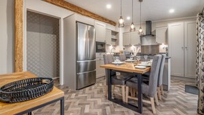A modern kitchen with a wooden table, chairs, and a built-in oven. - Lodge No 23 | Hot Tub | St Andrews Lodge Park (Strathkinness)