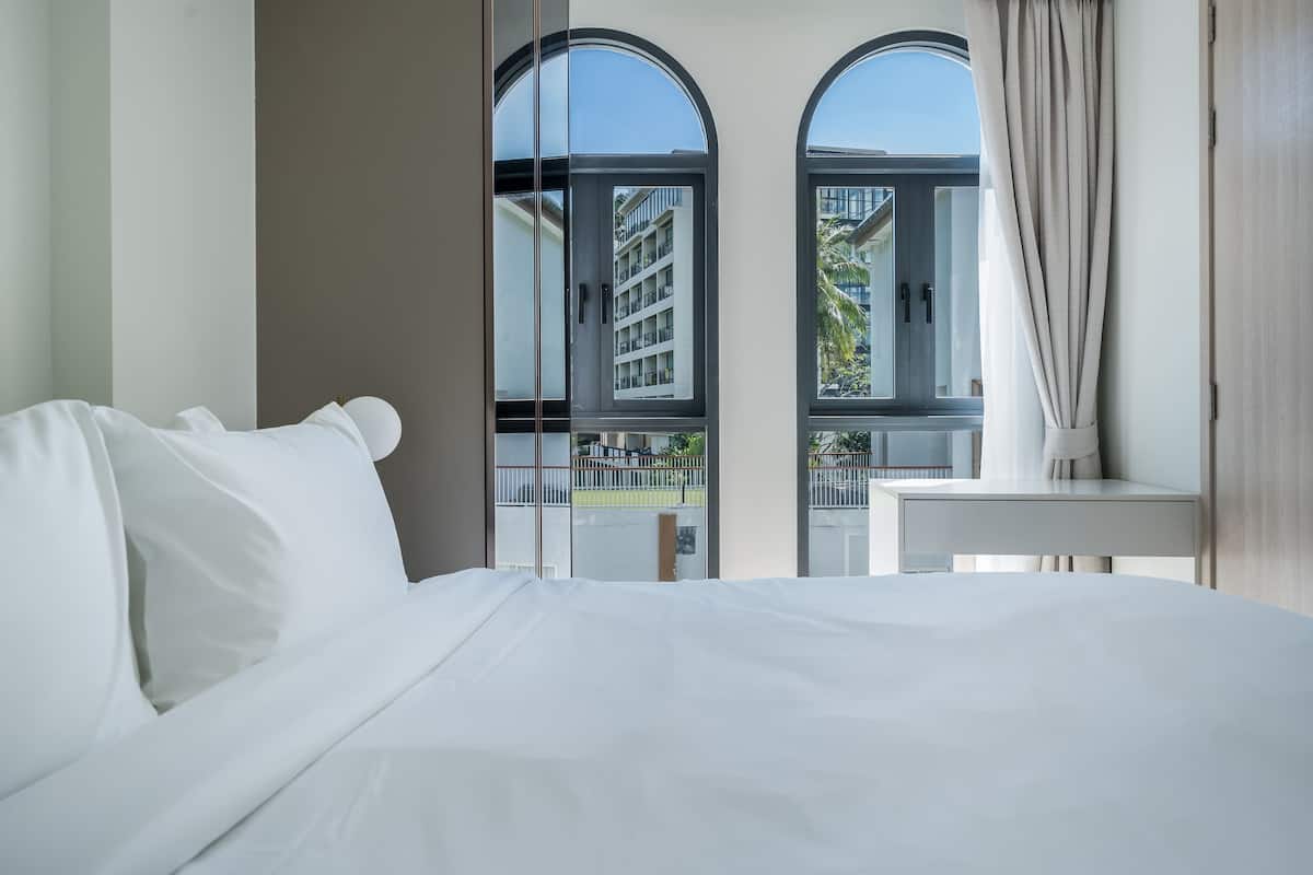 Habitación de hotel con una cama grande, una mesita y vistas a un edificio a través de ventanales arqueados.