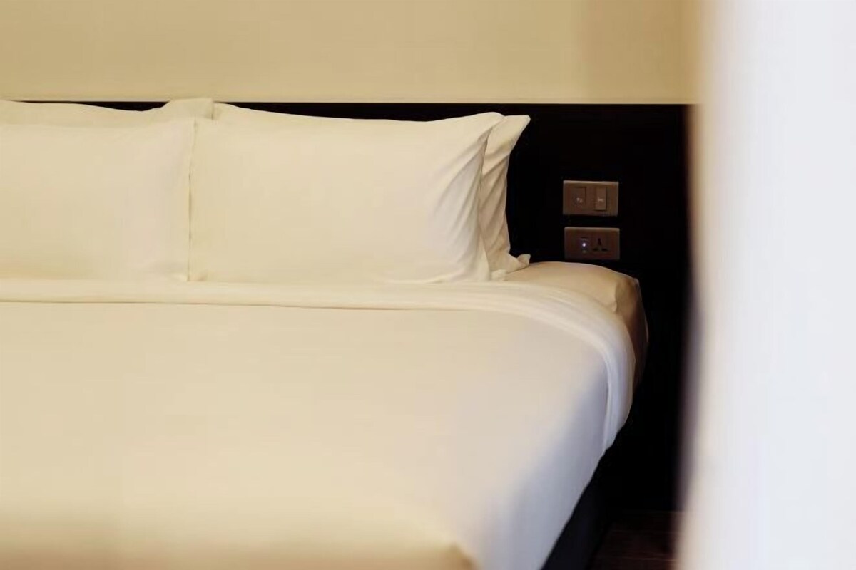 Un lit bien fait, avec du linge de lit blanc et une tête de lit sombre.