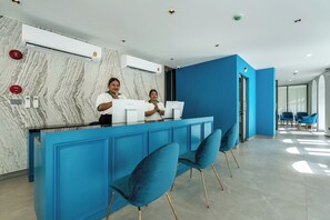 Un espace d’accueil avec un comptoir bleu, des murs en marbre et des chaises modernes.