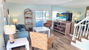 Una sala de estar con televisor, sofá, sillas, una mesa y una estantería.