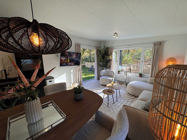Un salon moderne comprenant un coin repas, un téléviseur et une grande fenêtre donnant sur un jardin.