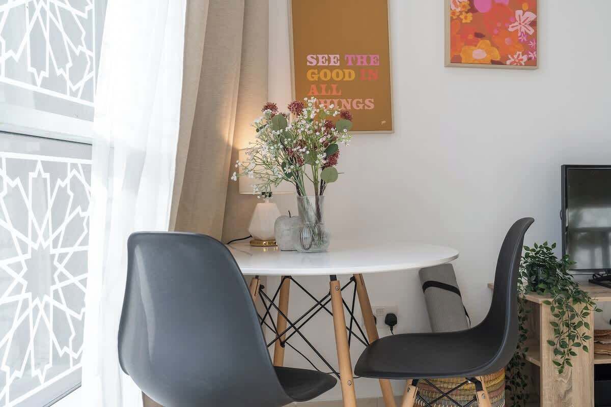 Ein moderner Essbereich mit einem runden Tisch, zwei schwarzen Stühlen und einer Blumenvase.
