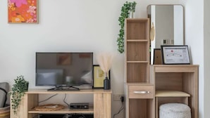 A modern living room with a wooden TV stand, a flat-screen TV, a small stool, a mirror, and a framed certificate.