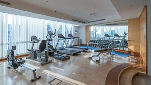 A modern gym with cardio machines, weight stations, and a large window offering a city view.