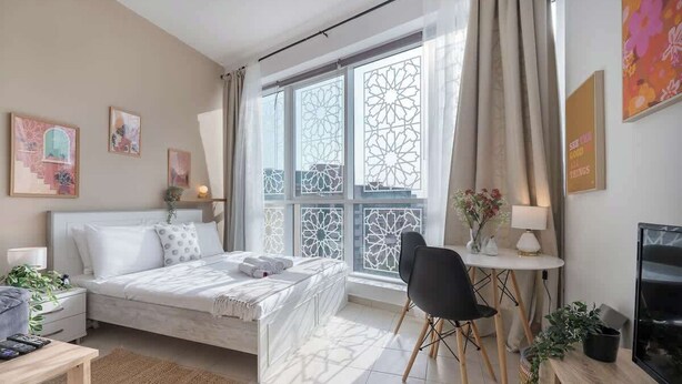 A modern bedroom with a large bed, a desk, a chair, and a TV.
