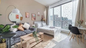 A modern living room with a sofa, coffee table, and a bed. There is a large window with decorative glass panels.