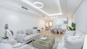 A modern living room with a sofa, armchairs, a glass coffee table, and a dining area with chairs and a table. - StayShort - Nice Villa in Gardenia, Jebel Ali for Family of 5! (Jebel Ali)