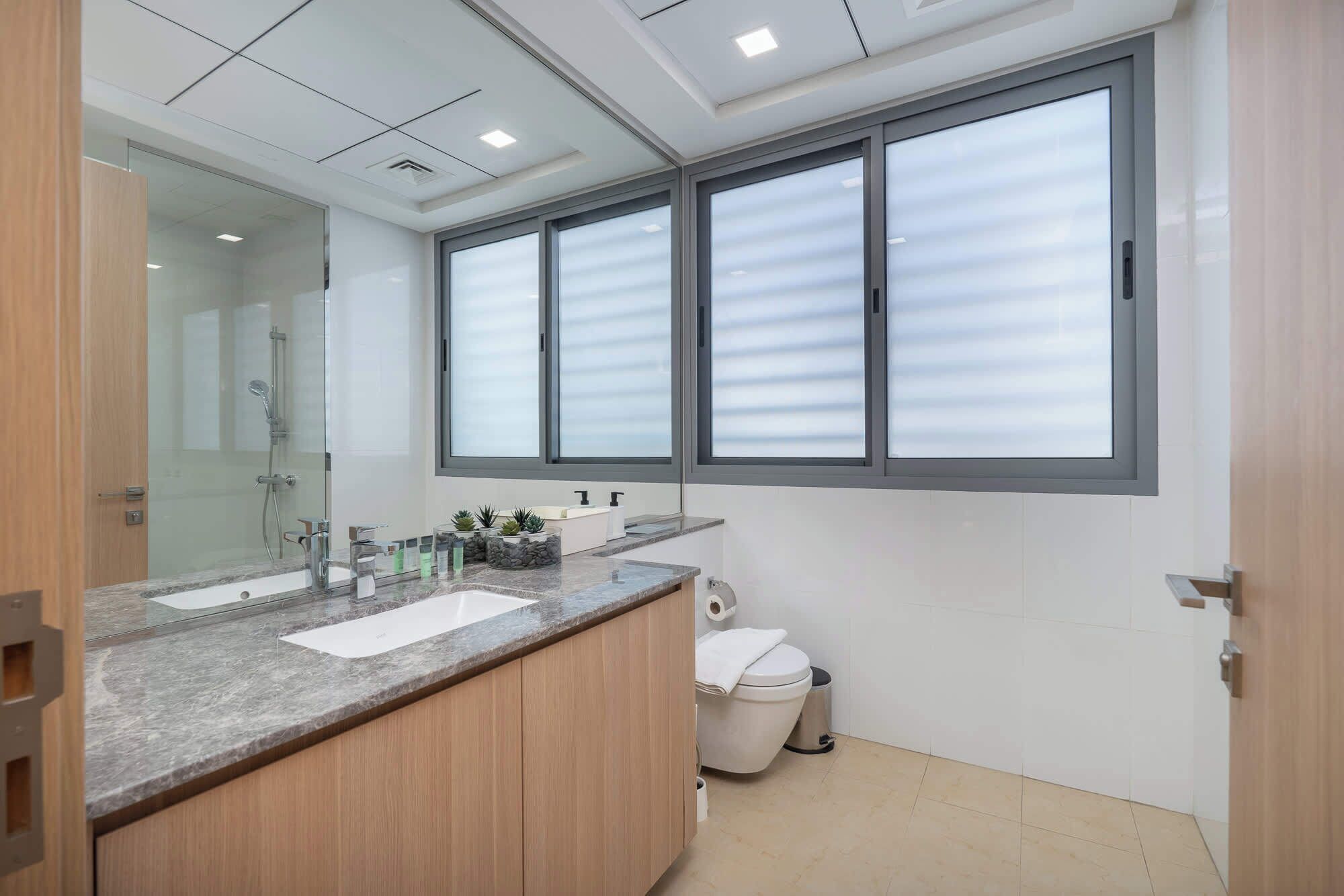 Une salle de bain moderne dotée d’une grande fenêtre, d’une douche, d’un lavabo et de toilettes.