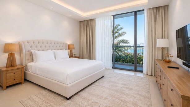 A modern hotel room with a large bed, a TV, a wooden dresser, and a balcony with a city view. - StayShort - Nice Villa in Gardenia, Jebel Ali for Family of 5! (Jebel Ali)