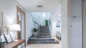 A modern interior with a staircase leading to a dining area, a potted plant, and a framed picture on a console table. - StayShort - Nice Villa in Gardenia, Jebel Ali for Family of 5! (Jebel Ali)