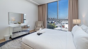 A modern hotel room with a large bed, a vanity with a mirror, and a view of the city through large windows. - StayShort - Nice Villa in Gardenia, Jebel Ali for Family of 5! (Jebel Ali)