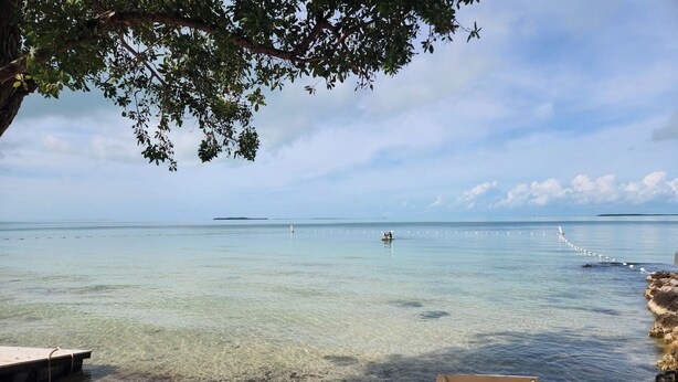 A beach with clear water, a wooden chair, and a table.