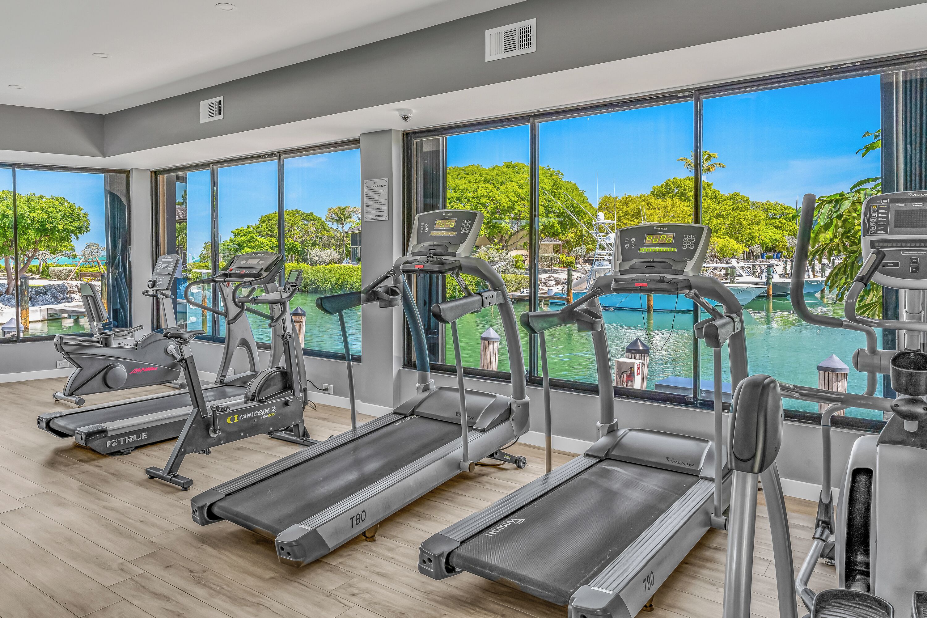 A gym with treadmills and exercise equipment, large windows with a view of a pool and trees.