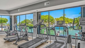 A gym with treadmills and exercise equipment, large windows with a view of a pool and trees.