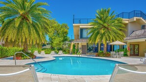 A swimming pool with palm trees, lounge chairs, and a building with a balcony.