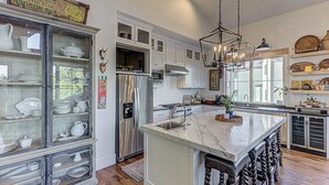A modern kitchen with white cabinets, a large island with a sink, stainless steel appliances, and a hanging light fixture. - LBJ Waterfront Escape | Private Dock & sleeps 16! (Kingsland)