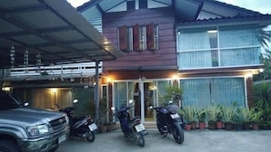 A two-story house with a covered garage and a motorcycle parked in front. - Napakarn (Mae Chan)