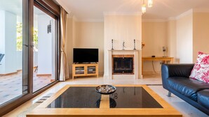 Een moderne woonkamer met een glazen salontafel, een leren bank, een open haard en een televisie op een houten kast.