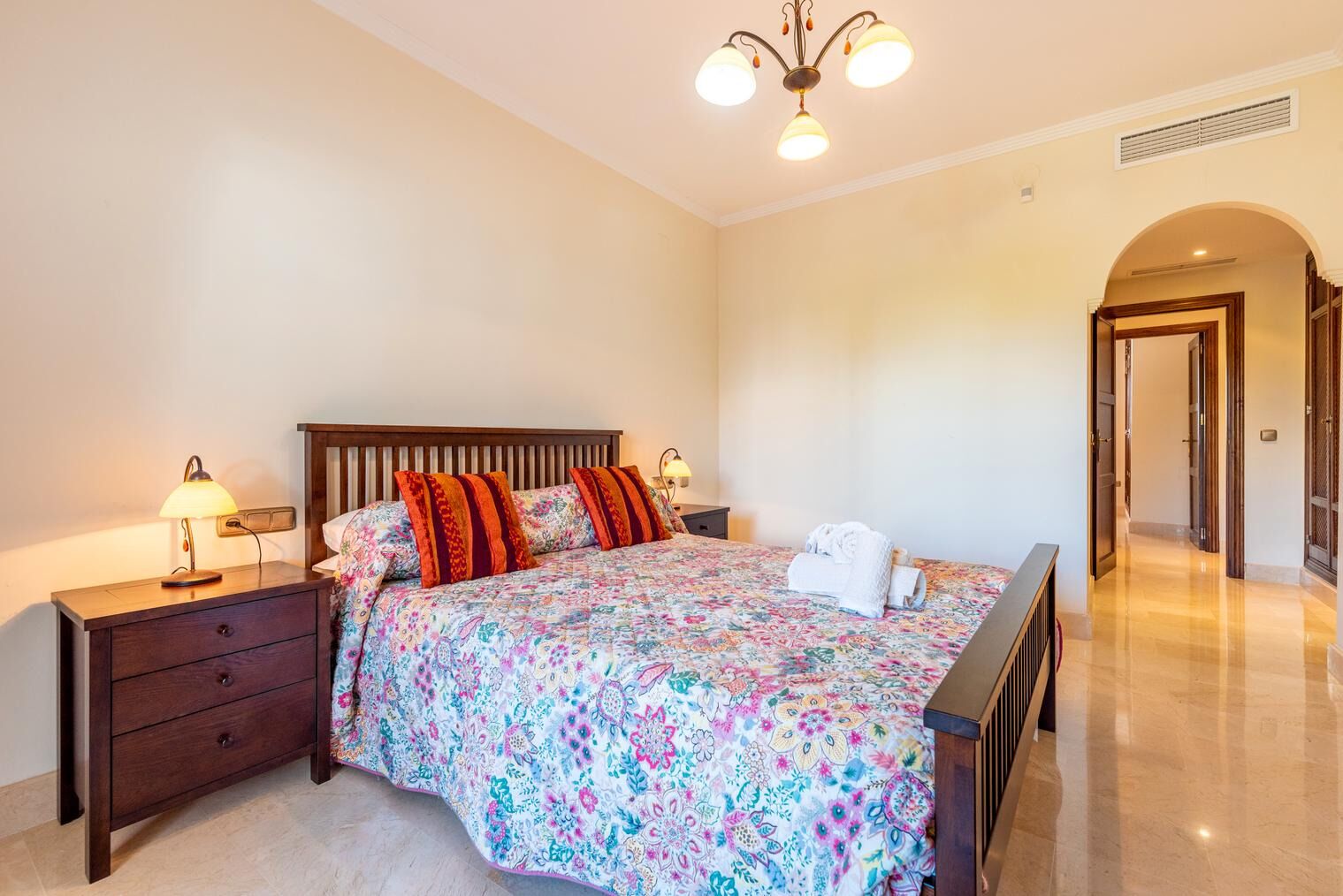 A bedroom with a bed, nightstands, a lamp, a chandelier, and a bathroom door.