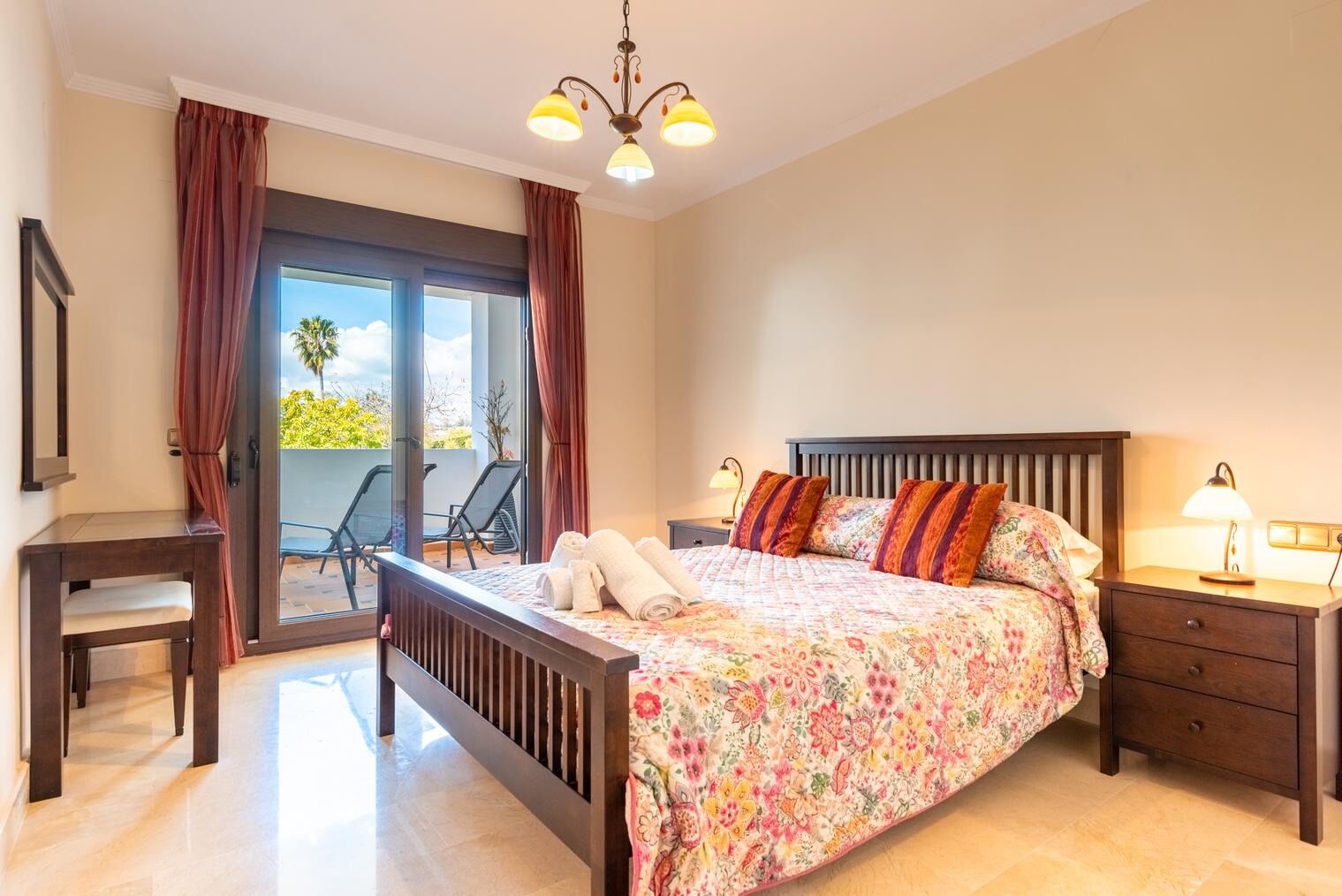 A bedroom with a bed, a desk, a chair, a nightstand, and a balcony with a view.