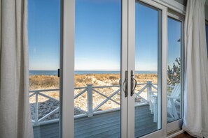 Une vue sur la plage depuis une chambre dotée d’une porte-fenêtre coulissante, de rampes blanches et de chaises de plage.