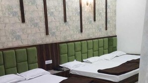 A hotel room with three beds, a green upholstered headboard, a marble floor, and a textured wall with vertical wooden slats. - Hotel SR Siddhivinayak  (Mathura)