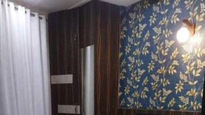 A modern bedroom with a large bed, a wooden headboard, a mirror, and a floral-patterned wall. - Hotel SR Siddhivinayak  (Mathura)