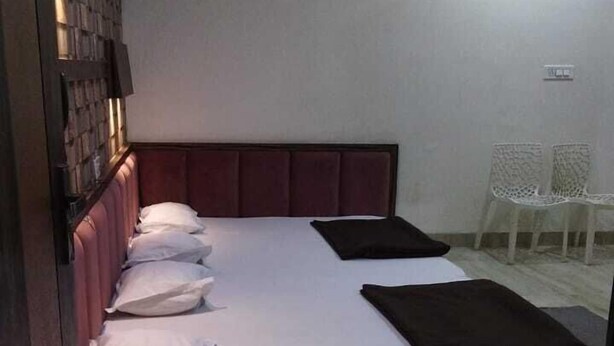 A single bed with a headboard, white bedding, and a dark-colored throw blanket. There is a ceiling fan and an air conditioning unit on the wall. - Hotel SR Siddhivinayak  (Mathura)